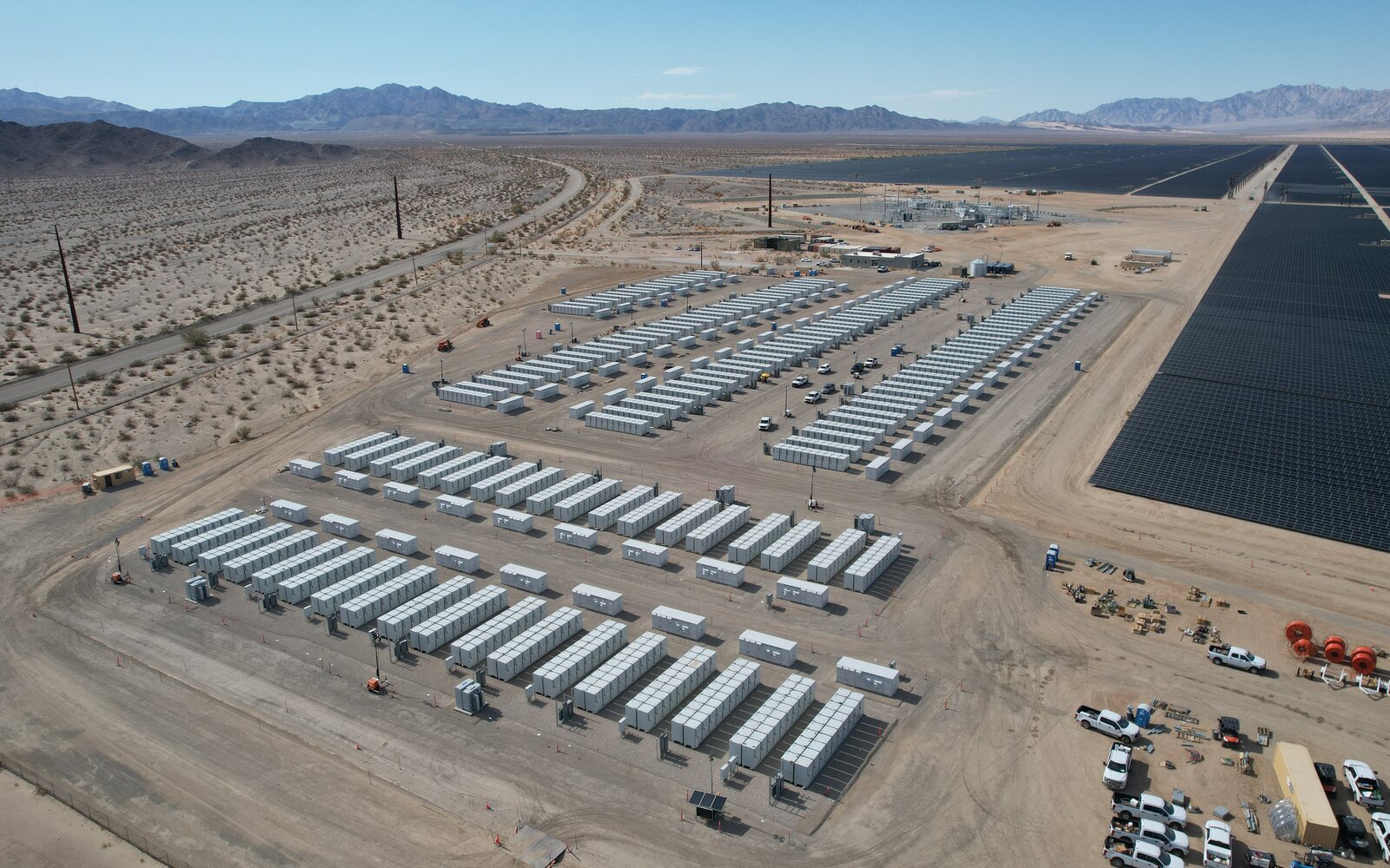 Aerial view of utility-scale battery storage units beside a desert solar farm.