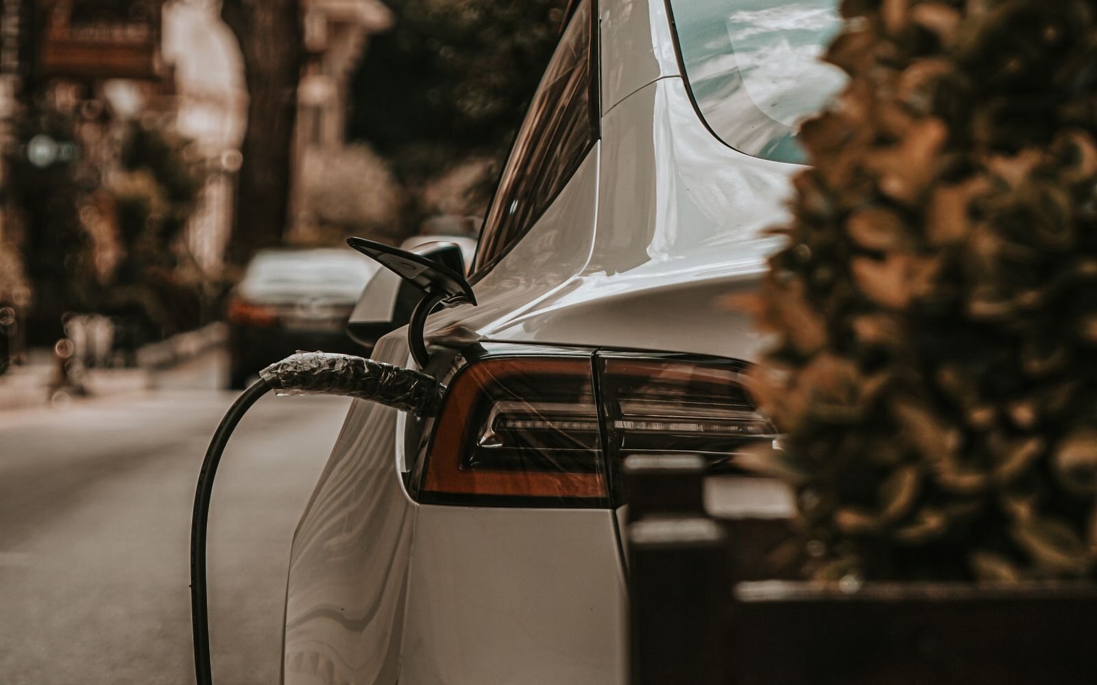 Charging cable connected to the rear of a white electric car on a residential street.