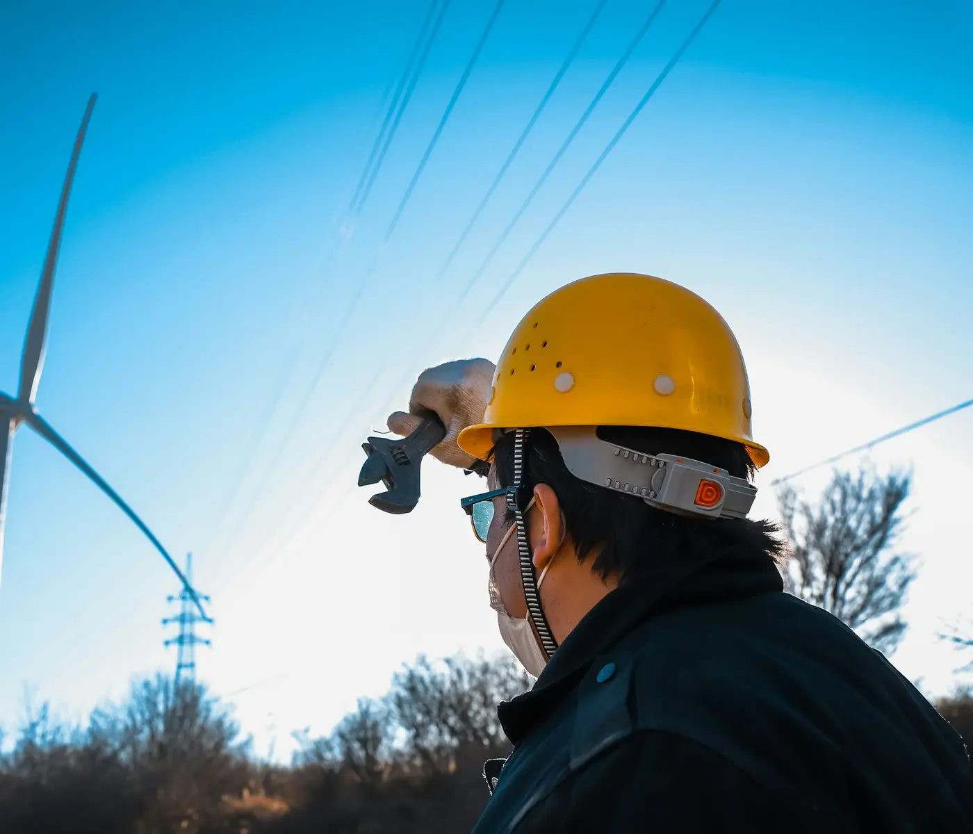 An engineer in a hard hat below a wind turbine.