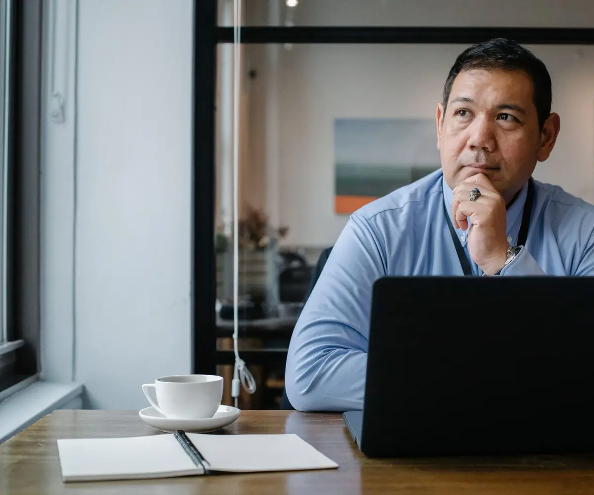 A man at a laptop with his hand at his chin, weighing something up.