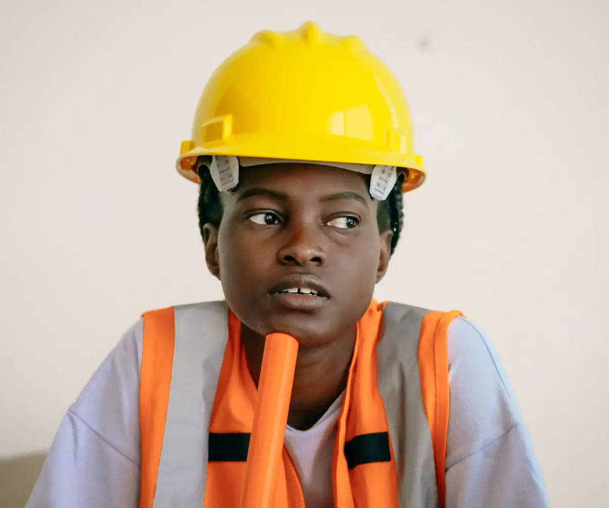 An engineer in a hard hat and high visibility vest, lost in thought.